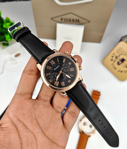A Fossil chronograph watch with a black dial and black leather strap, held in a person's hand. The watch features a rose gold-toned case and matching rose gold hands and markers.